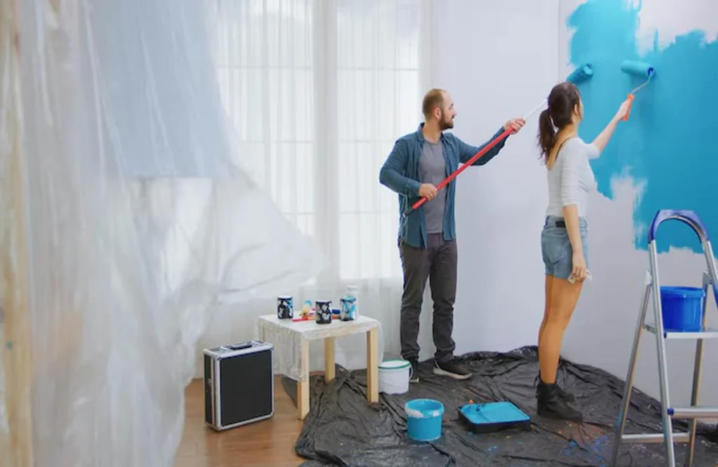 A couple painting an apartment wall with blue paint, demonstrating one of the 10 common apartment painting mistakes that ruin the finish when not done right.