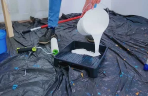 A person pouring high-quality paint into a tray, preparing for application. This paint is ideal for humidity areas, offering protection and durability for long-term use.