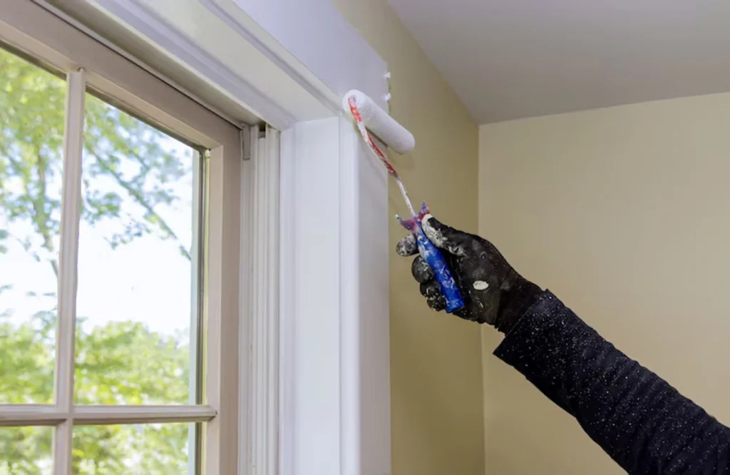A person applying the best paint for humidity areas to a window frame. This high-quality paint helps prevent damage caused by moisture, providing long-lasting protection for your walls.
